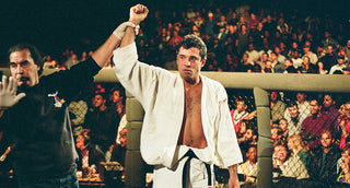 Royce Gracie raises his arm in victory inside the UFC octagon wearing a white gi